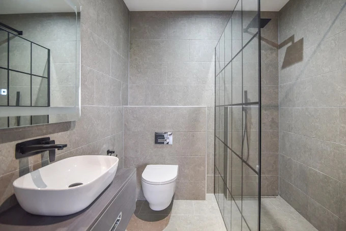 Walk-in shower ensuite with stone tiling and wall-hung WC by SES Renovations